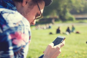 A man browsing through his smartphone in a park.